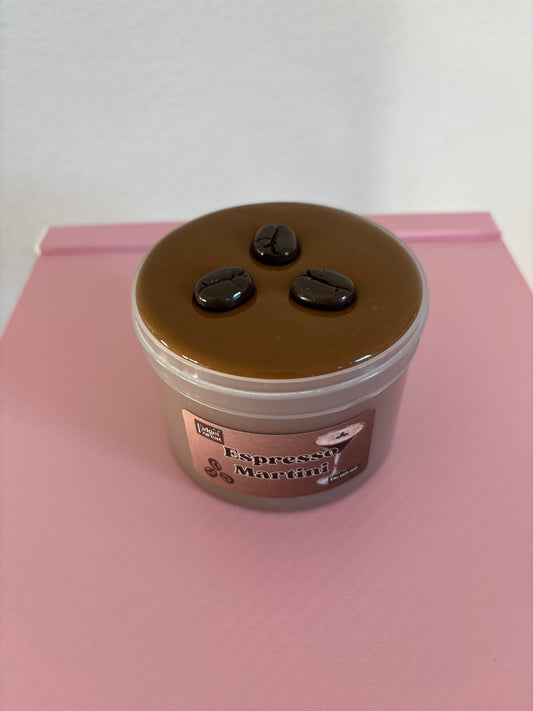 Brown slime with coffee bean charms on top, in a container labeled “espresso martini” on a pink background