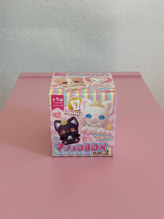A mystery box for Mashlo Box Surprise Character squishies Vol. 2 featuring cute cartoon cat illustrations, photographed on a pink surface against a white wall.
