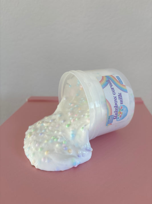 White slime with rainbow foam beads spilling out of container labeled “Rainbow Cereal Milk” with a pink background