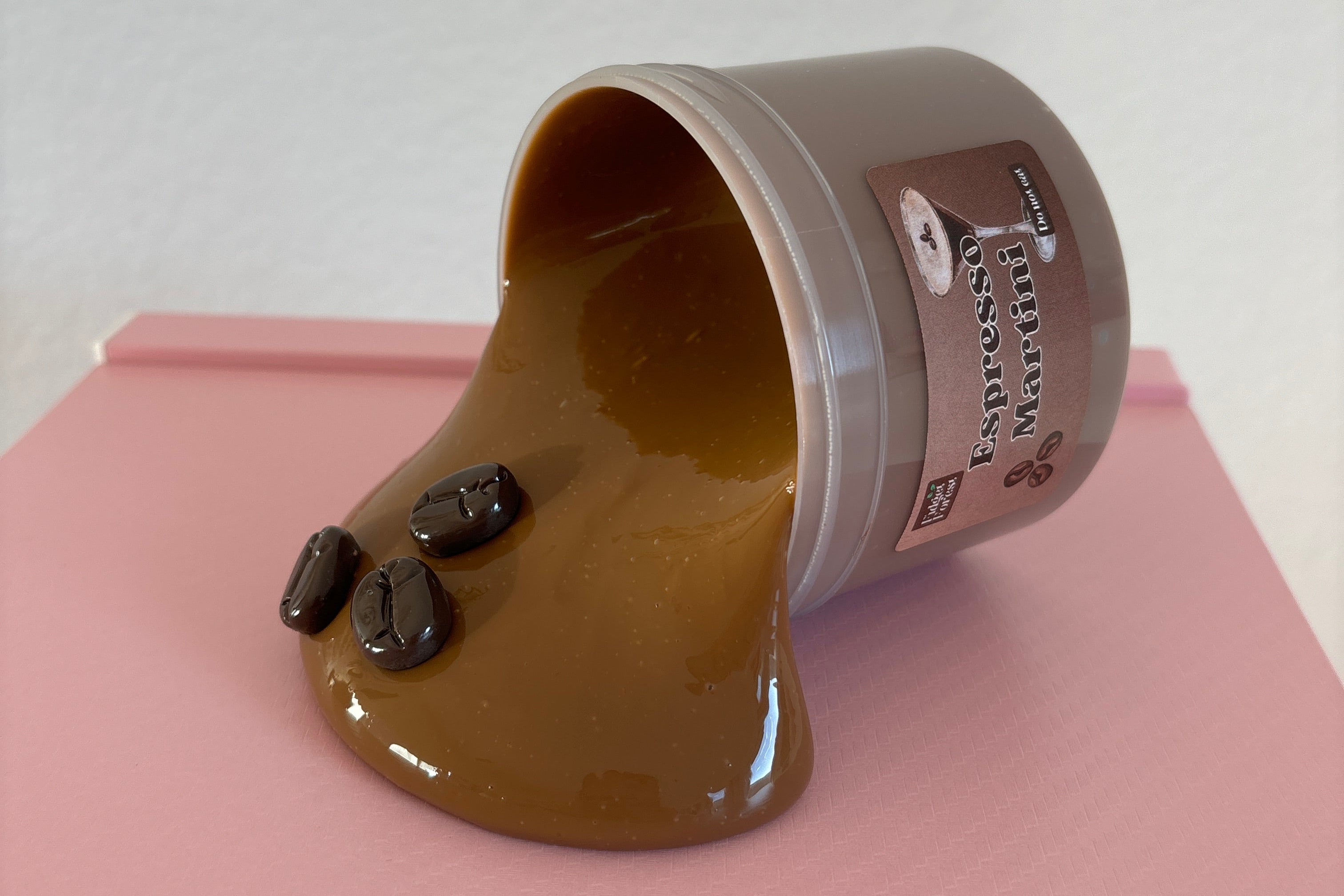 Brown Slime with 3 coffee bean charms spilling out of container labeled "espresso martini" on a pink and white background