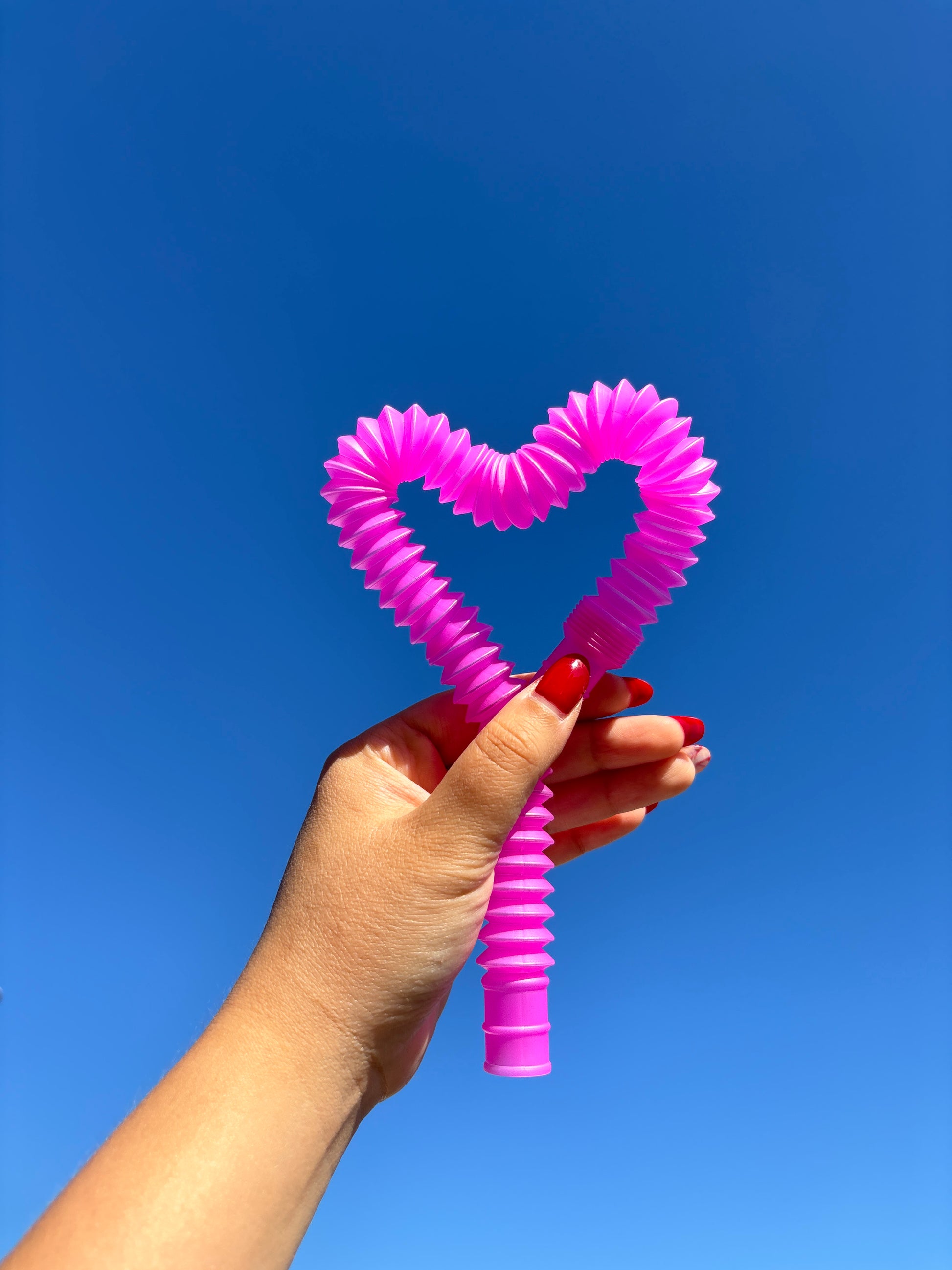 Hot Pink / Magenta Pop tube shaped into a heart being held in front of a blue sky background