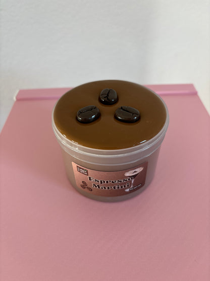 Brown slime with coffee bean charms on top, in a container labeled “espresso martini”  on a pink background