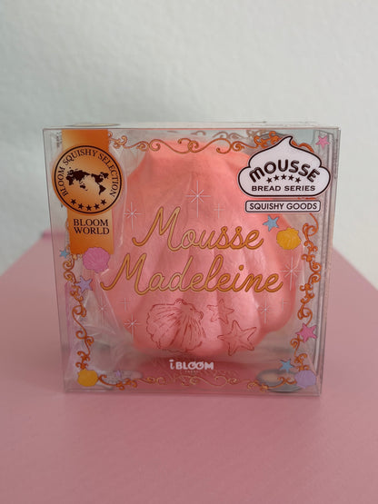 A clear plastic package containing a pink squishy toy shaped like a madeleine cookie, with decorative gold foil text and branding including 'Mousse Madeleine' by the brand IBLOOM.