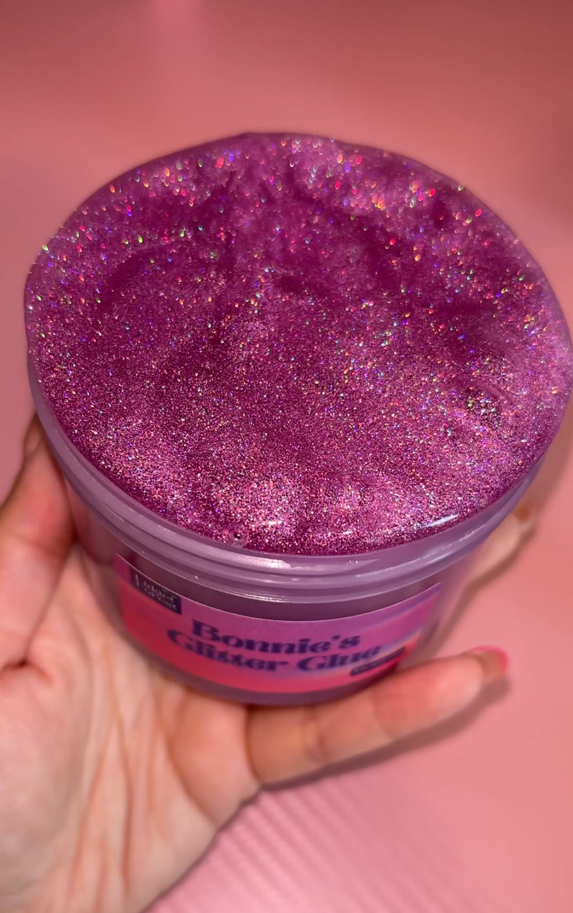 Purple Holographic Glitter slime in container labeled “Bonnie’s Glitter Glue” with pink background 