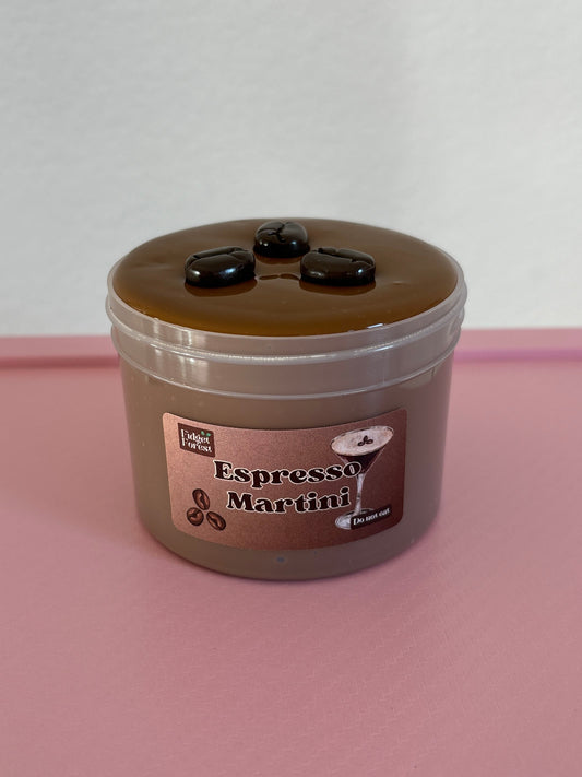 Brown slime with coffee bean charms on top, in a container labeled “espresso martini”  on a pink background
