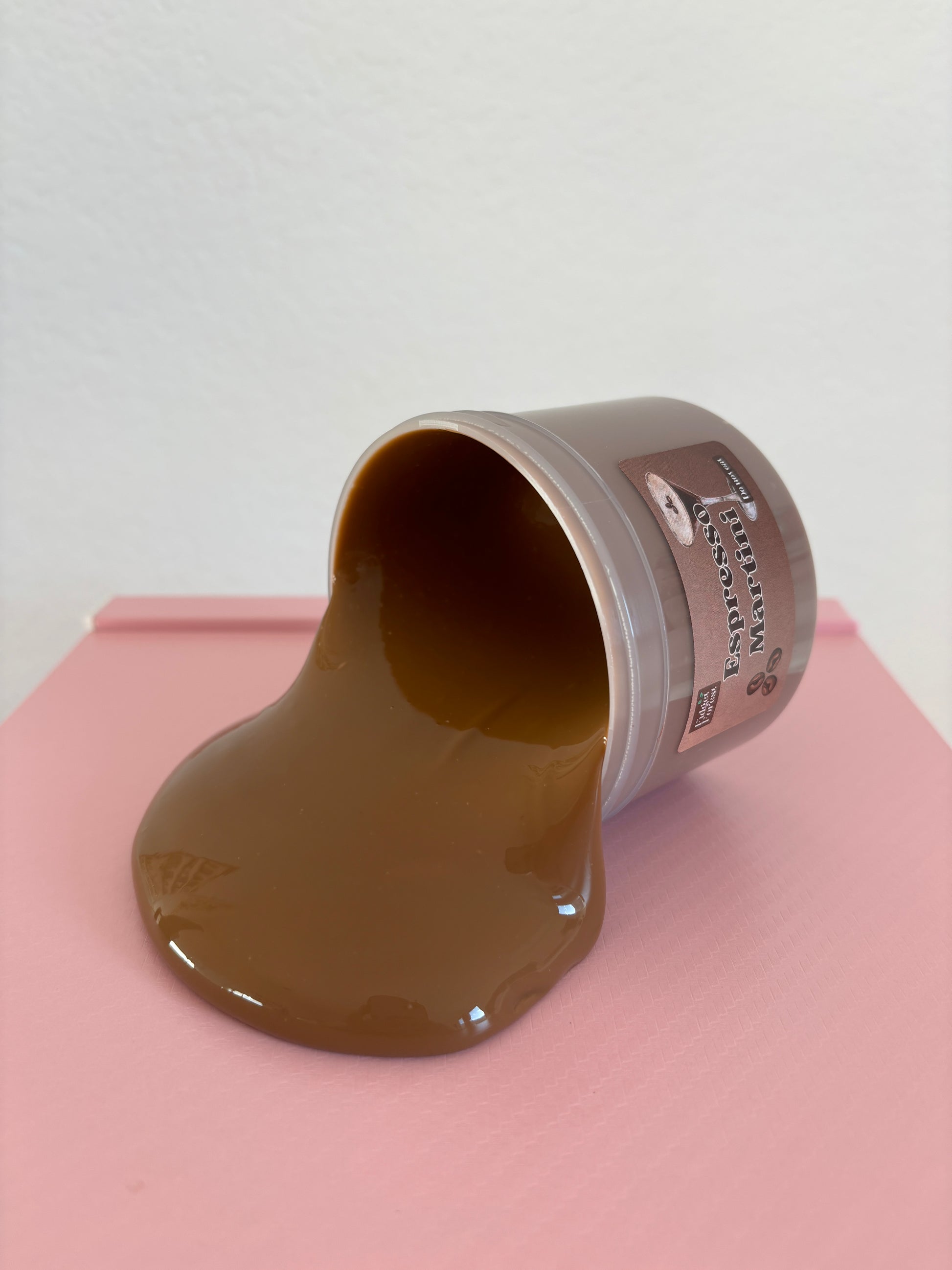 Brown slime spilling out of a container and onto a table, labeled “espresso martini”  on a pink and white background