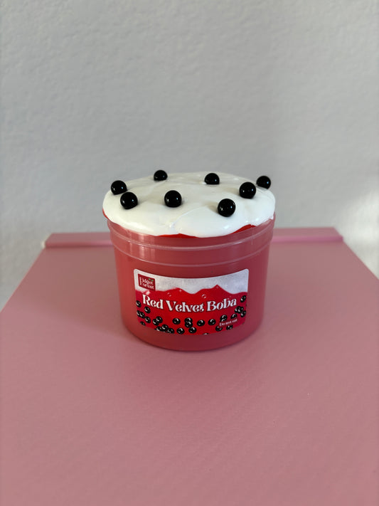 Red and White Slime with black beads labeled “Red velvet boba” in a container against a pink background