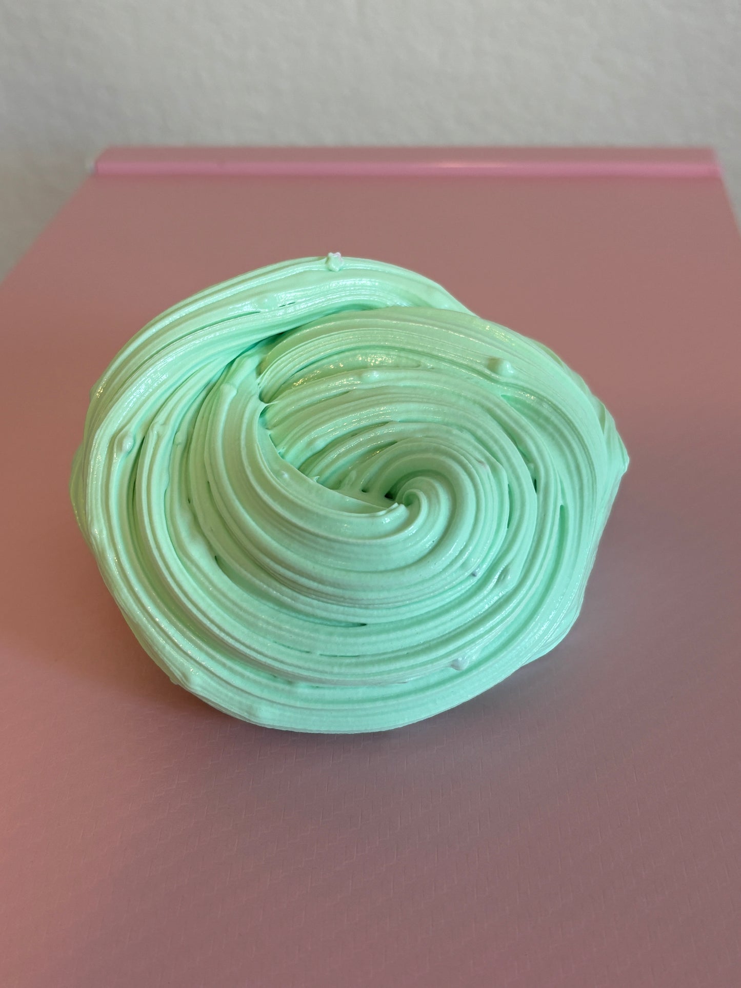 Mint green slime with glitter mix ins swirled into a round swirl shape