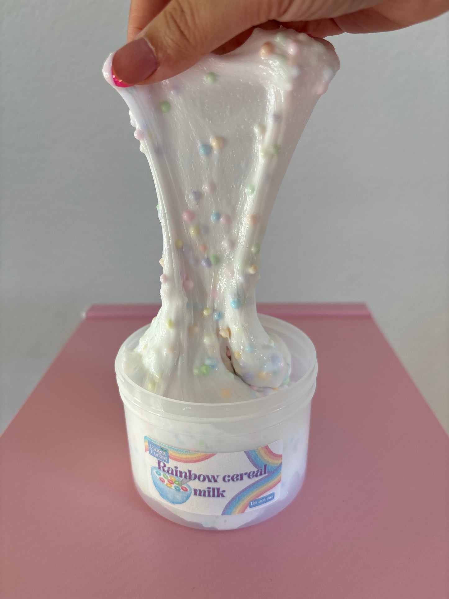 Hand pulling a white slime with rainbow beads up against a pink background