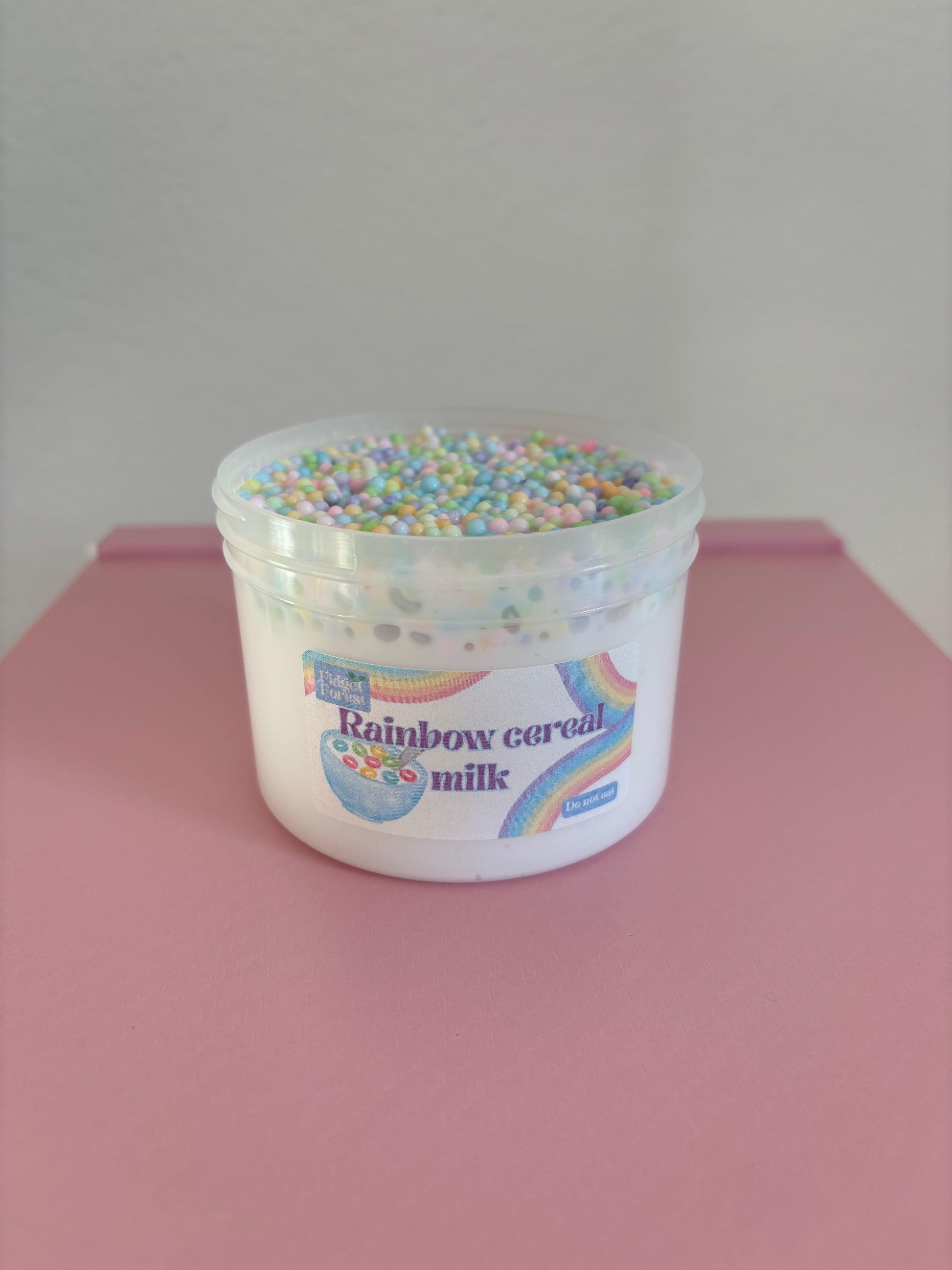 Container of rainbow cereal milk slime with a pink background
