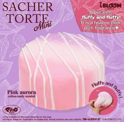 A pink fluffy squishy toy shaped like a mini cake, labeled 'SACHER TORTE Mini' and 'Pink aurora cotton candy scented'. The image features a purple background with floral patterns, promotional text, and a circular logo for 'iBLOOM'.