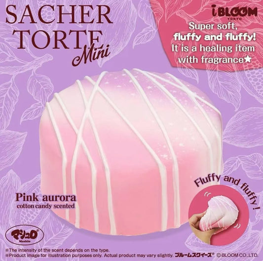 A pink fluffy squishy toy shaped like a mini cake, labeled 'SACHER TORTE Mini' and 'Pink aurora cotton candy scented'. The image features a purple background with floral patterns, promotional text, and a circular logo for 'iBLOOM'.