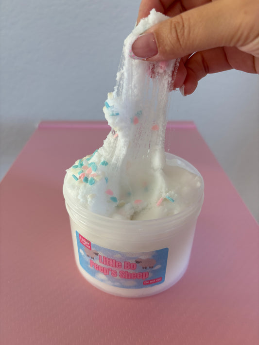 White Cloud Slime in container labeled “Little Bo Peep’s Sheep” with cloud sprinkles being pulled up by hand in front of pink background