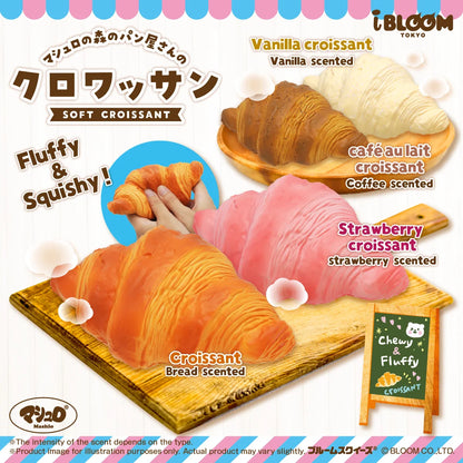 Promotional graphic for Bloom Tokyo soft croissant squishies, showing three scented croissant squishies: vanilla, café au lait, and strawberry. A hand is shown holding a vanilla croissant.