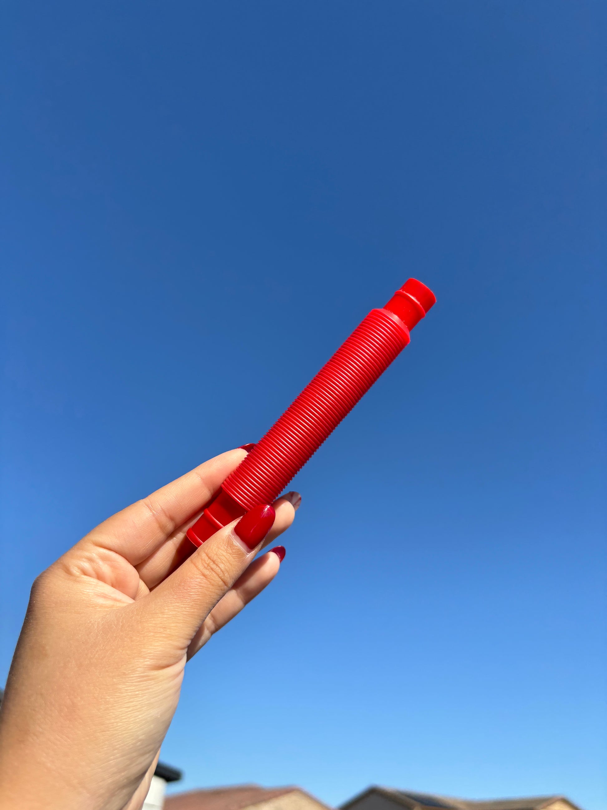Red pop tube being held up in front of sky background