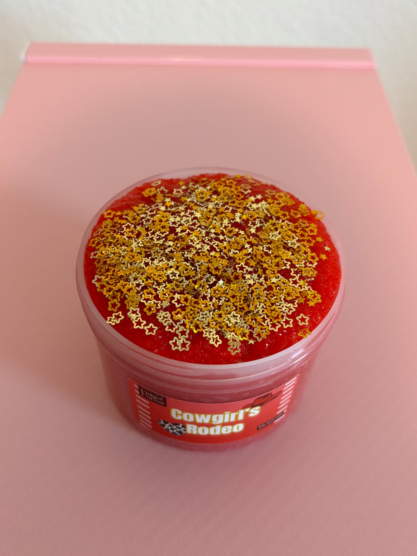 Red snow fizz slime in container with gold star glitter on top, in front of pink background 