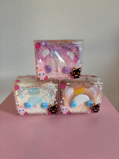 Three packaged Nyan Nyan Roll-Cat squishies stacked on a pink surface against a light wall. The top package contains a pink squishy with purple circular accents, and the two bottom packages contain brown and white-colored squishies with blue and yellow accents.