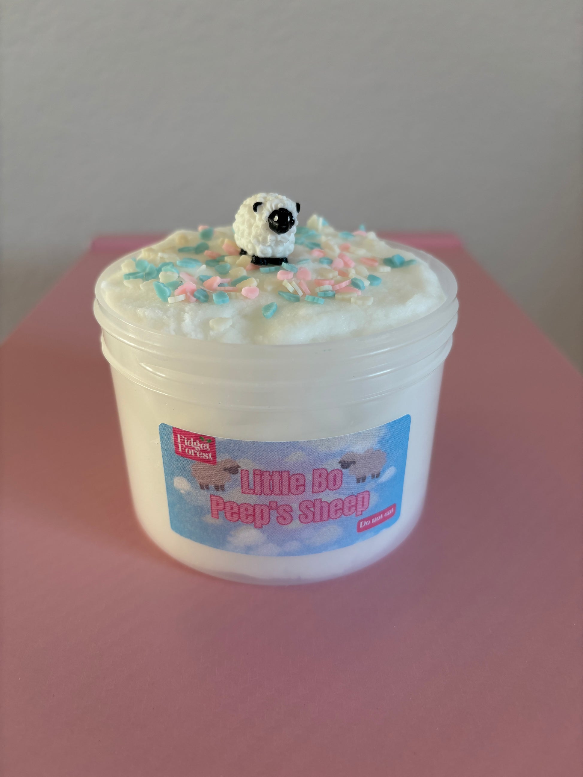 White Cloud Slime in container labeled “Little Bo Peep’s Sheep” with cloud sprinkles and Sheep charm on top in front of pink background