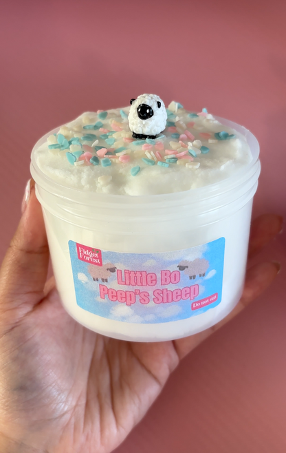 White Cloud Slime in container labeled “Little Bo Peep’s Sheep” with cloud sprinkles and Sheep charm on top in front of pink background