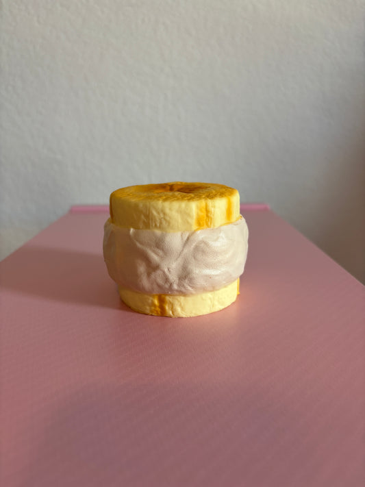 Side view of the Hachimi Banana Cream Puff Squishy toy, showing a thick layer of textured white cream filling sandwiched between two golden-yellow pastry slices. Centered on a white and pink background.